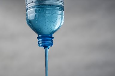 Upside down plastic bottle with blue liquid running out